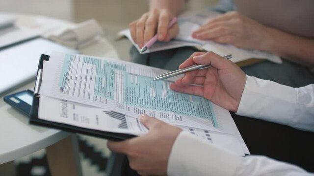 Closeup of unrecognizable female hands of financial advisor running pen through paper documents analyzing tax returns
