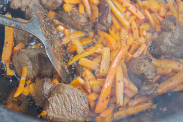 Cooking pilaf in a cauldron on the grill outside in the summer