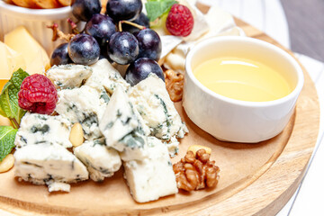 Board with different types of cheese. Cheeses mix set dor blu chedar parmesan brie honey sauce finger bread and grape on wooren palte. Restaurant menu breakfast plate. Healthy snack assortment.
