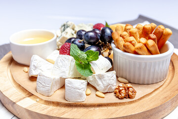 Board with different types of cheese. Cheeses mix set dor blu chedar parmesan brie honey sauce finger bread and grape on wooren palte. Restaurant menu breakfast plate. Healthy snack assortment.