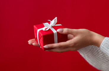 Female hands  holding red gift box with white ribbon and bow on the red background. Christmas and New Year holidays. Valentine's Day and Birthday. Surprise, greeting, celebration, present. Isolated