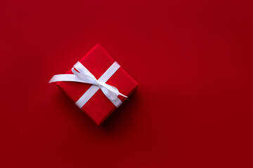 Red gift box with white ribbon and bow on the red background. Banner, copy space, flat lay and top view. Christmas and New Year concept. Valentine's day and Birthday. Celebrating