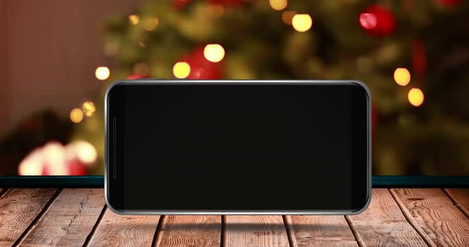 Animation of blank smartphone screen with out of focus christmas tree on wooden surface