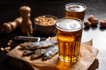 Close up. Cold beer in a glass and snacks on a wooden table on a dark background. Dried fish and nuts. Fast food in local brewery, pub. Oktoberfest. Still life, rustic.