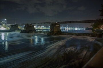 Eine Staustufe mit Schleuse und Fu&szlig;g&auml;ngerbr&uuml;cke an einem Fluss bei Nacht