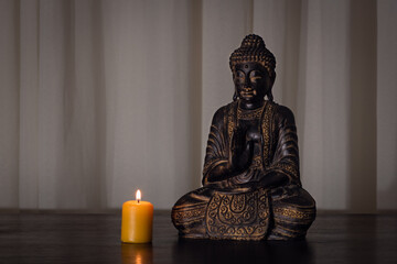 Buddha statue with burning candle on wooden table with soft textured background and dark environment. Spirituality, buddhism and religion concepts 