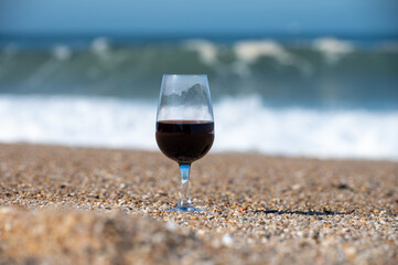 Tasting of different fortified dessert ruby, tawny port wines in glasses on sandy beach with view on waves of Atlantic ocean near Vila Nova de Gaia and city of Porto, Portugal