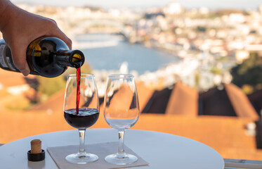 Pouring of fortified dessert ruby, tawny port wines in glasses with view on Douro river, porto lodges of Vila Nova de Gaia and city of Porto, Portugal