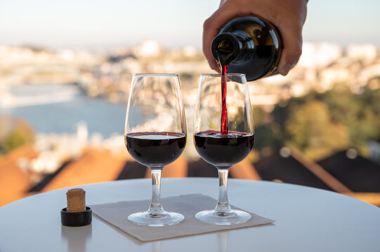 Pouring of fortified dessert ruby, tawny port wines in glasses with view on Douro river, porto lodges of Vila Nova de Gaia and city of Porto, Portugal