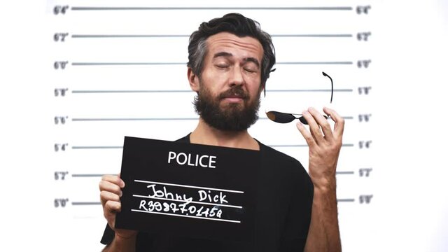 Handsome bearded man in sunglasses posing for mug shot at police station