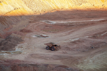 A large dump truck surrounded by dirt, background lit by sunset © Cavan