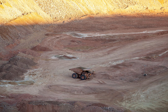 A large dump truck surrounded by dirt, background lit by sunset