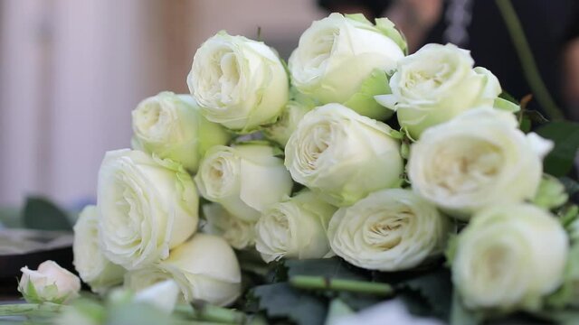 A florist girl, puts individual roses in a bouquet of white roses, which lies on the table. Preparing a bouquet for the client's order.