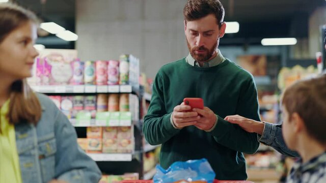 Busy bearded parent caucasian businessman father using smartphone talking to colleagues chatting online ignoring his family on food shopping grocery store.
