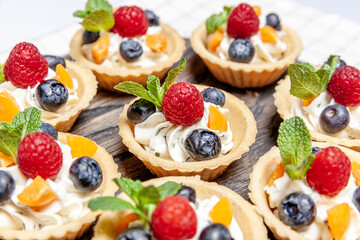 Fruit and berry tartlets dessert assorted on wooden tray. Closeup of delicious pastry sweets pies colorful cakes with fresh natural raspberry blueberry and cheese cream. French bakery catering.
