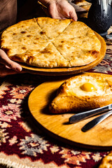Tasty Imeretian Khachapuri. Khachapuri Cheese Pie on a wooden plank in the man's hand. Adjarian khachapuri in front. Caucasian Kitchen. Vertical Orientation