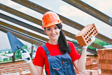 portrait of female woman mason hold in hands red brick with hole and metal trowel against metal...