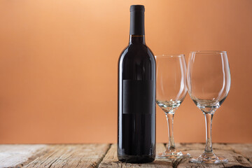 Bottle of red wine with empty glasses on rustic wooden table on beige background. Concept of alcoholic drink. Photo for advertising and product promotion. Space for text.