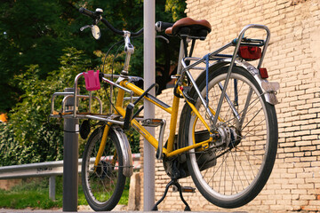 A vintage yellow bicycle parked on a street near a park of trees.