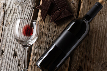 Bottle and glass with remain of red wine and dark chocolate on rustic wooden table on white brick...