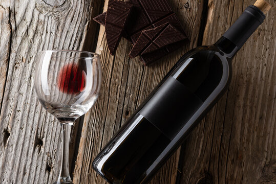 Bottle and glass with remain of red wine and dark chocolate on rustic wooden table on white brick background. Concept of alcoholic drink. Photo for advertising and product promotion. Space for text.