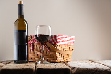 Bottle and glass with red wine with picnic basket on rustic wooden table on gray background....