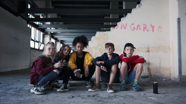 Group of teenagers gang with smartphone indoors in abandoned building, looking at camera.