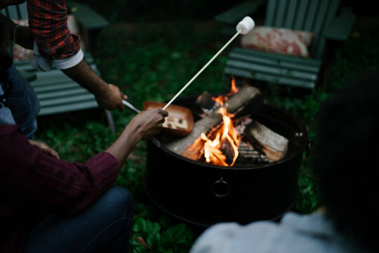 Black friends gathering around fire-pit roasting marshmallows and eating smores