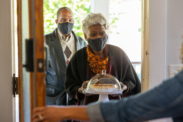 Grandmother and grandfather greet family for Thanksgiving wearing mask