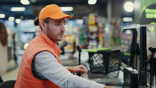 Portrait of nice-looking young professional man cashier wearing orange uniform working at grocery store modern supermarket cash register consumer services concept.