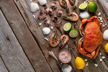 Top view of assorted seafood. Cooked crab, baby octopuses and tiger shrimps served with sea salt, lime and seashells on rustic wooden background. Seafood concept. Delicious healthy meal.