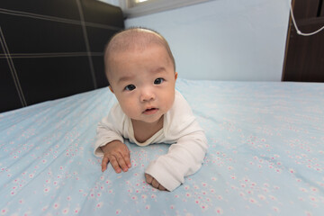 Adorable and happy Chinese baby boy on tummy time on bed. Newborn child relaxing in bed