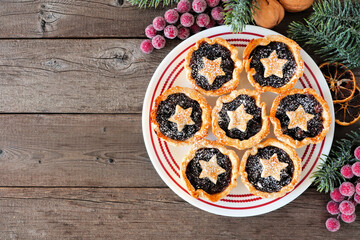 Plate of Christmas mincemeat tarts. Top down view table scene over a dark wood background.