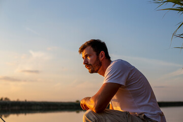 Portrait of a handsome man looking at the river sunset.