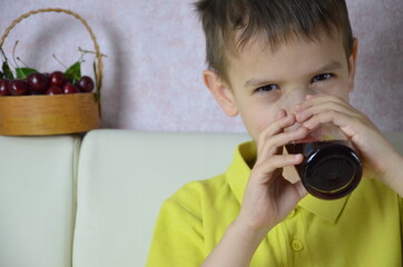 Cute little boy drinking juice at home, cherry juice drinks from a bottle or a glass with a straw.