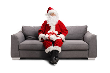 Full length portrait of a santa claus sitting on sofa and holding a gift box - Powered by Adobe