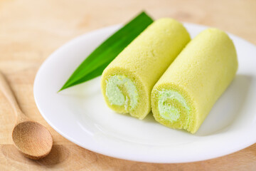Pandan roll cake with pandan leaf on white dish and spoon on wooden table