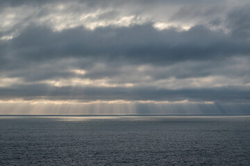 Sun rays coming down from the clouds over the ocean. View of the horizon line on a cloudy sunset