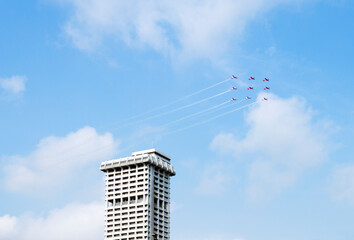 A squadron of aircraft performing an airshow with beautiful formation passing by tall building on a...