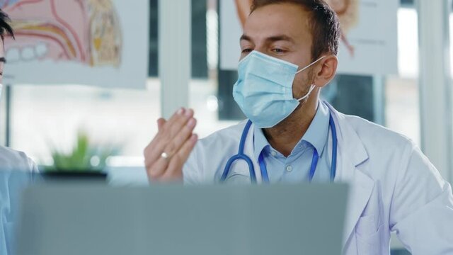 Two multi-race diverse doctors wearing face masks discussing disease influenza lung infection xray image communicating cooperating in hospital office.