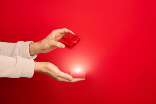 Female hand hold open red small jewelry box on red background.