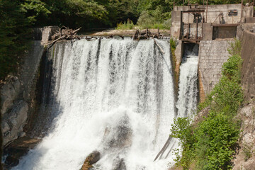 Old abandoned hydroelectric power plant against a backdrop of green trees