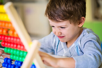 Cute Caucasian baby boy feeling bored and frustrated while playing with an abacus at kindergarten