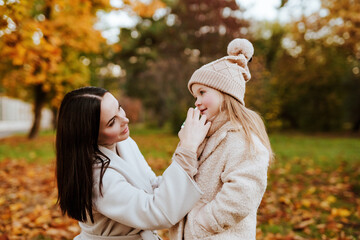 Fototapeta premium mom buries spray in nose of little daughter in hat and scarf in autumn Park