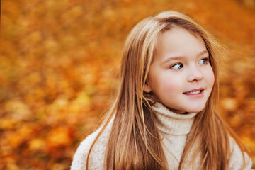 Portrait of blue-eyed little girl in wight autumn sweater in autumn park