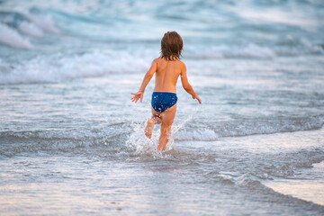 Fototapeta na wymiar Vacation with children. Happy child running in the sea. Kid boy having fun on the beach. Summer kids.