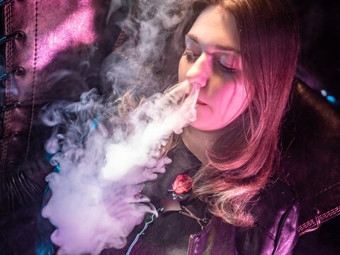 The girl releases smoke from her nose. A woman releases cigarette smoke. Smoke comes from the nose of a woman. Concept - student smokes cigarettes. Woman with closed eyes blows steam.