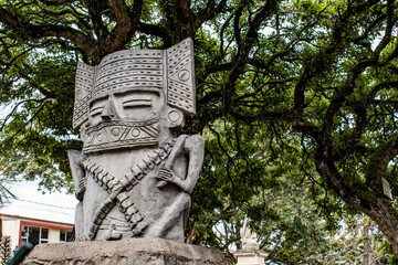 A picture of a medium size grey statue with tree branches and green leaves behind it. Photo taken...