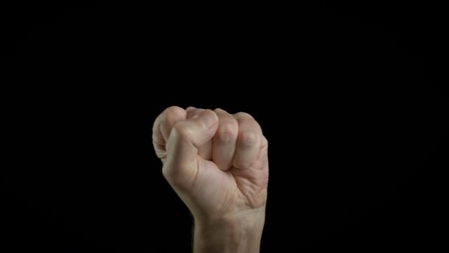 Agressive man. A person with aggression makes a fist on the black background.