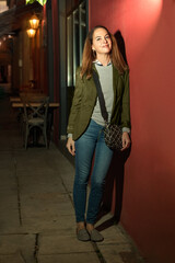 Woman standing leaning on a red wall, outdoors.